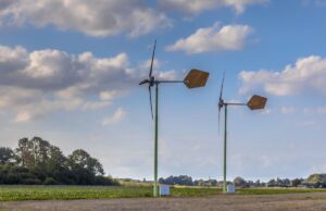 Two small wind turbines in an open field with blue sky and clouds in the background