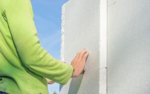 A homeowner touching a sheet of RetroFoam Insulation on the corner of a home's exterior