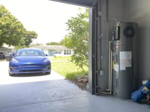 a new heat pump water heater installed in a garage next to a parked tesla model 3
