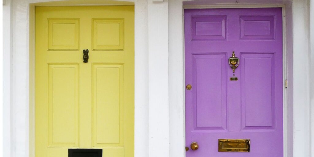 Two doors on neighboring houses, the left hand side door is yellow and the right hand side door is purple.