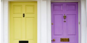 Two doors on neighboring houses, the left hand side door is yellow and the right hand side door is purple.