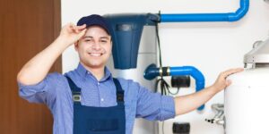 Technician in blue overalls, blue cap and blue shirtin front of a water heater.
