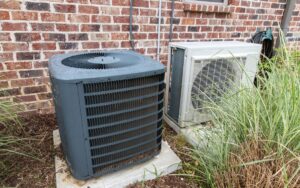 Side view of a mini-split's compressor unit next to a central AC outside a home