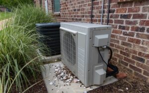Side view of a mini-split's compressor unit next to a central AC outside a home