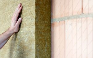 Closeup of a hand installing a Rockwool insulation batt on top of a brick wall