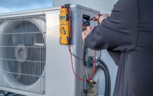 A technician on a rooftop adjusts the configuration of a mini-split compressor