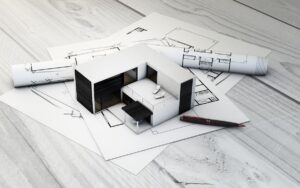 A model modular home sits atop a table with blueprints underneath it