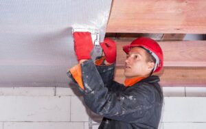A serviceman installs a vapor barrier on the ceiling in a basement