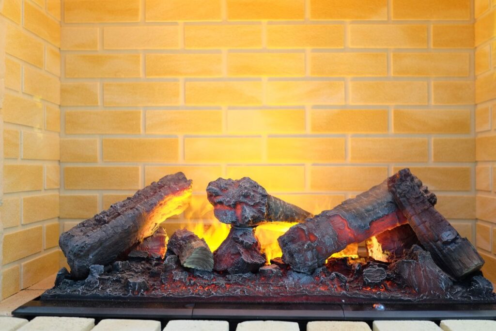 An electric fireplace in a mock hearth that is glowing to demonstrate the effect you can expect after electrifying your fireplace. The fire is made to look like wood and there is brown brickwork behind.
