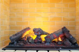 An electric fireplace in a mock hearth that is glowing to demonstrate the effect you can expect after electrifying your fireplace. The fire is made to look like wood and there is brown brickwork behind.