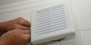 White grille of the type used to cover exhaust fans vs. ventilation fans, with a man's hands prying the cover free.