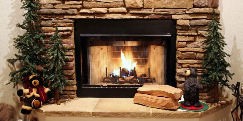 A chimney and fireplace with stone surround. The fire is lit and there are animal decorations on the hearth.