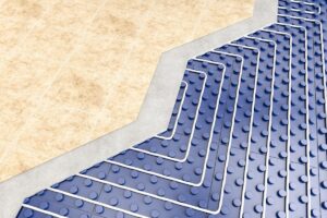 A beige tiled floor with a cutaway chowing the grout and an underfloor radiant heating system beneath.