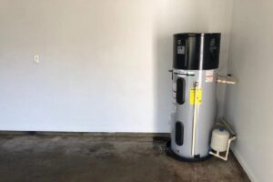 A hot water heater in the corner of a garage with concrete floor and white walls.