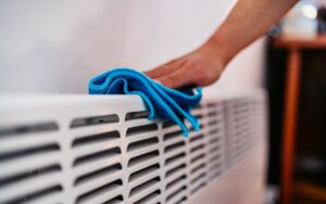 Closeup on the vent of a an wall radiant heater being wiped down by a homeowner