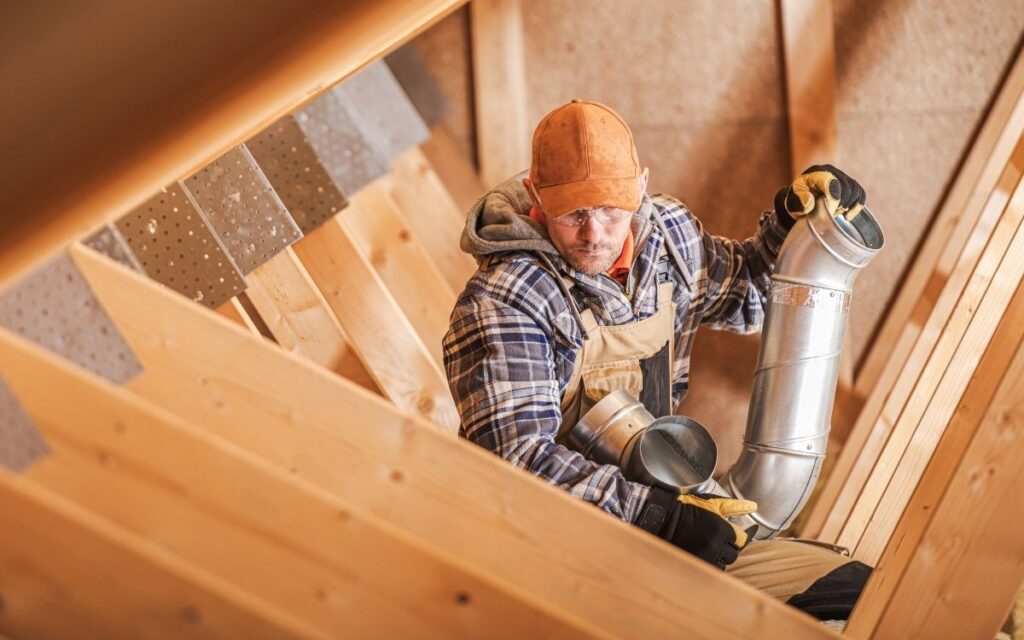 A technician install ducting of a home ventilation system in an attic