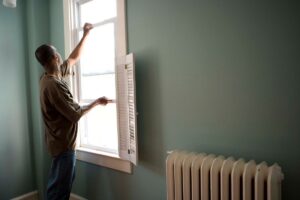 A homeowner conducting a home ventilation test inspects a window for leaks and mold