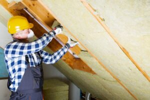 A worker installing insulation between the rafters in a roof.