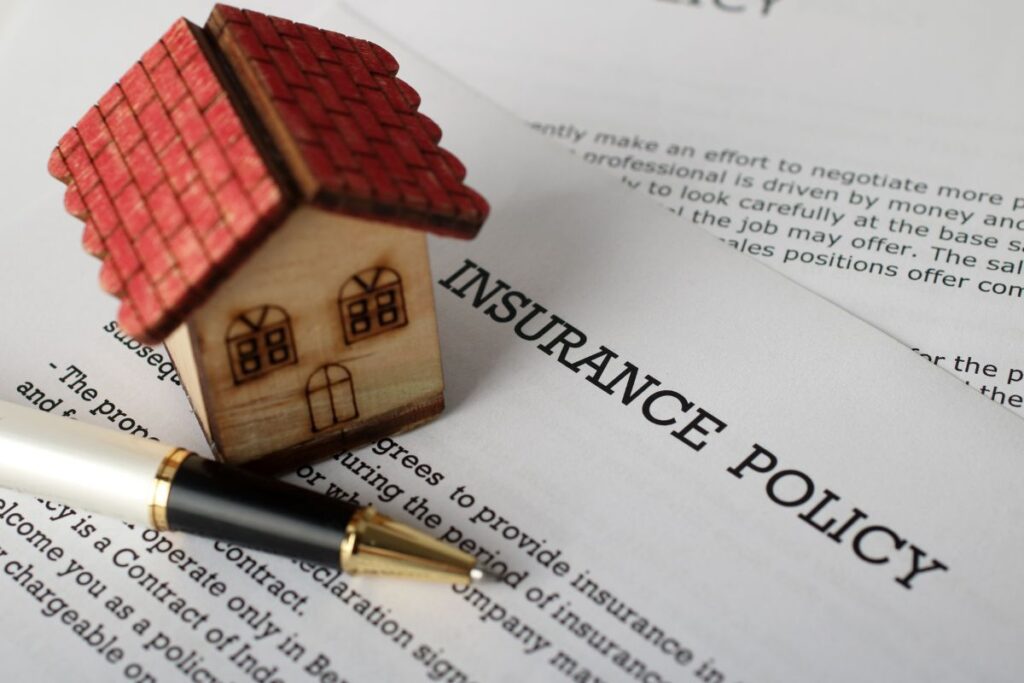 A pen and model home rest on a homeowners insurance policy on a table