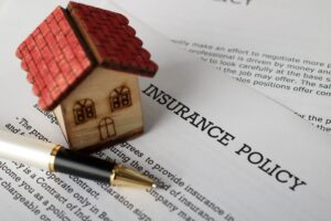 A pen and model home rest on a homeowners insurance policy on a table