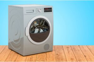 A heat pump tumble dryersitting on a wooden floor with a blue wall behind it.