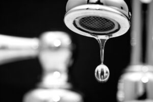 Closeup on the end of a leaky faucet with a bead of dripping water suspended from it