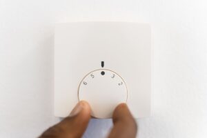 A thermostat for a radiant heating panel with a hand turning it to adjust the temperature.