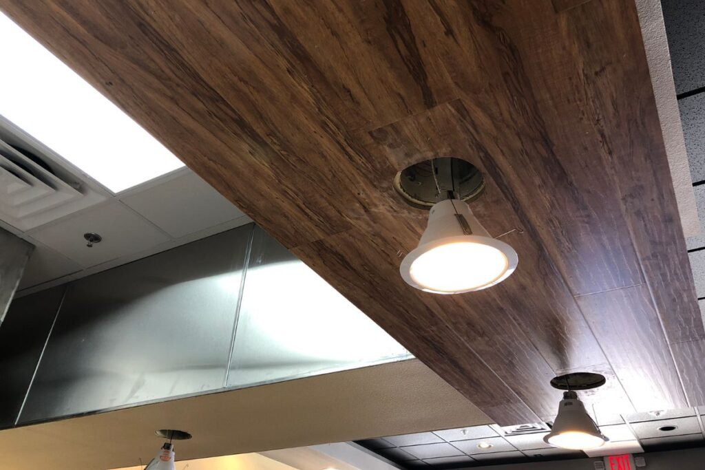 a row of recessed can lights hanging from a wood paneled-ceiling readied for installation