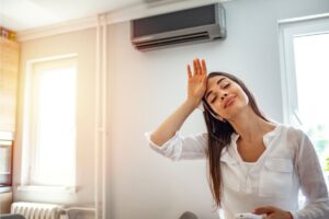 A homeowner pictured in front of her AC's living room evaporator wiping sweat off her brow