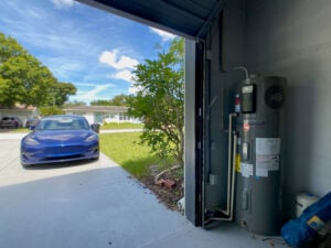 a blue tesla model 3 on the left with a rheem hybrid heat pump water heater on the right in a garage