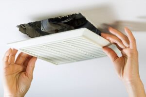 Closeup on a homeowner's hands removing a bathroom exhaust fan
