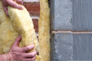 Closeup on a homeowner gripping a a fiberglass insulation batt barehanded as he installs it on a wall