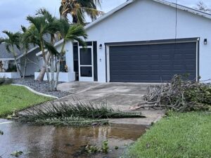 a white house with trees down and flooding in the driveway after hurricane ian