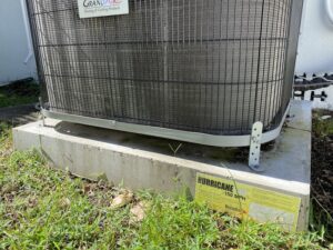 a concrete hurricane pad strapping down an air conditioning unit outside