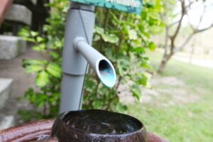 A pipe from a greywater system that recycles water from an air conditioner dripping water into a bowl outside a home