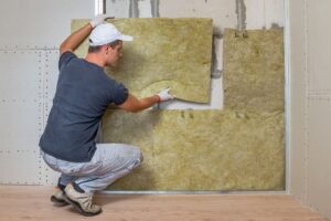 A homeowner appliying Rockwool insulation batts on a wall, a form of green insulation
