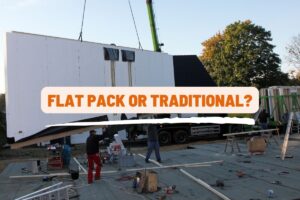 two men help move a wall panel into place held by a crane on a concrete foundation