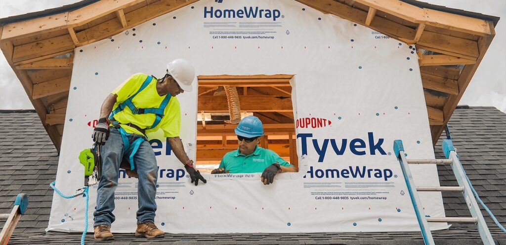 Two workers installing a Dupont Tyvek HomeWrap on the second story exterior of a home