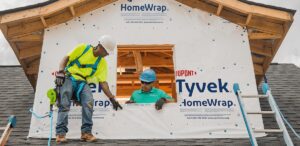 Two workers installing a Dupont Tyvek HomeWrap on the second story exterior of a home